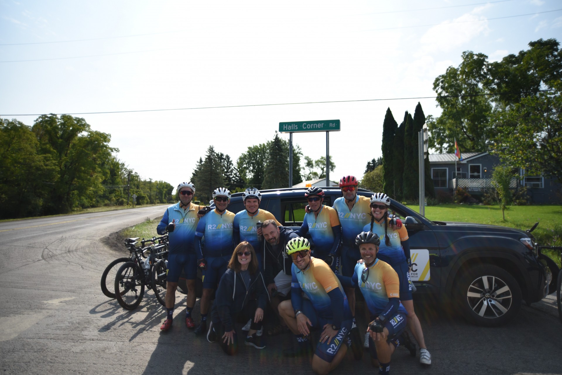 support crew members pictured with riders at a stop in front of a car on a sunny day with trees in the background