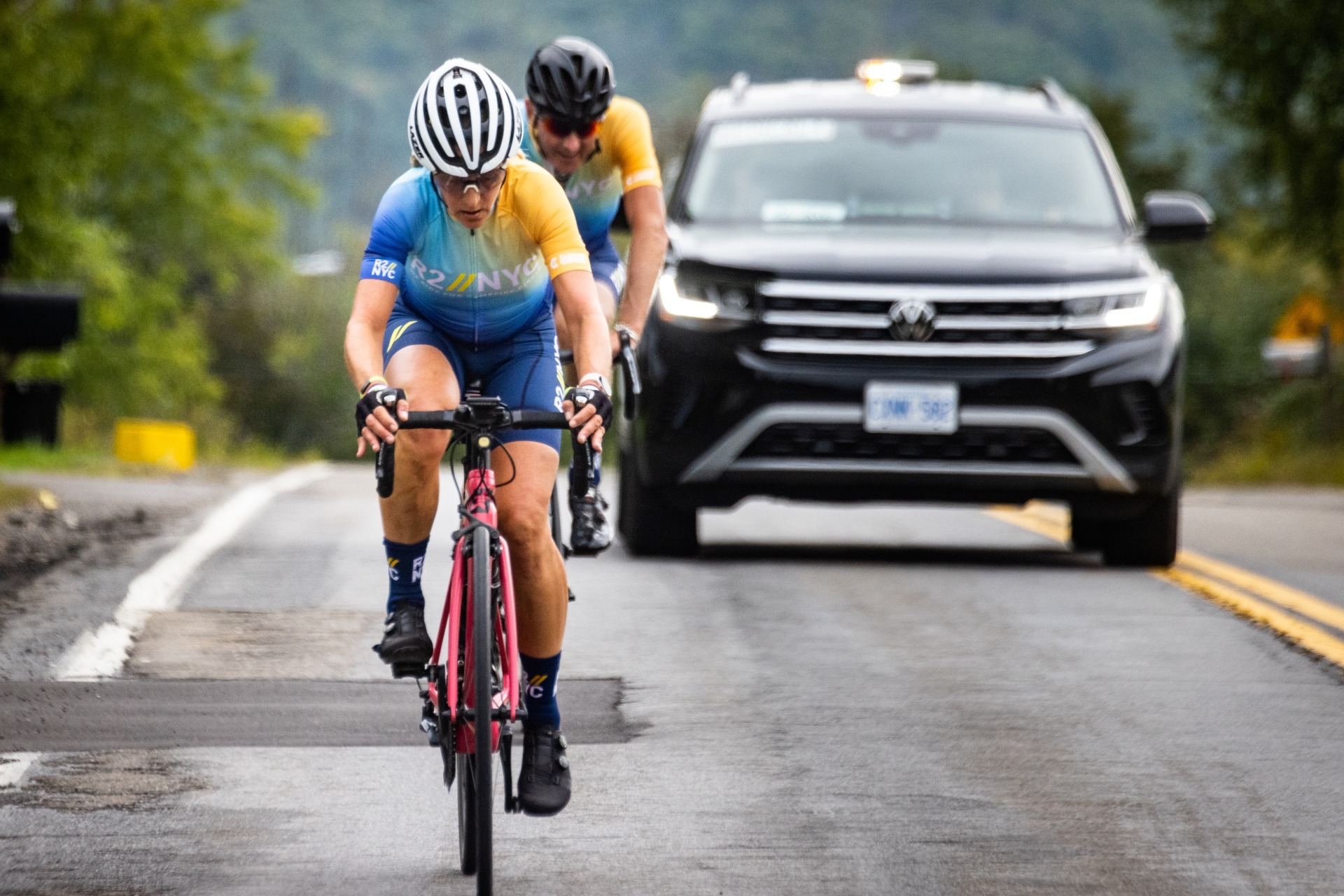 two cyclists riding in front of Volkswagen support car
