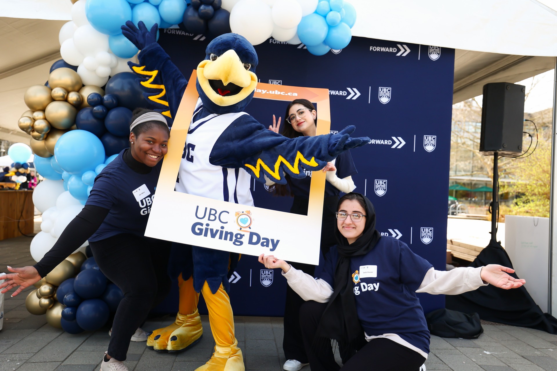 Group of cheerful volunteers posing with Thunder at UBC Giving Day event.