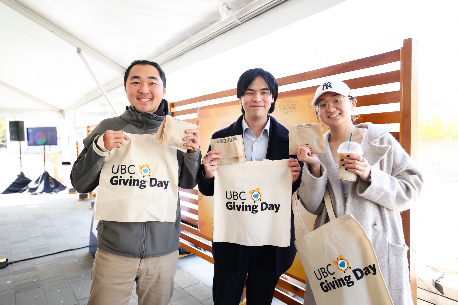 Three happy individuals holding UBC Giving Day tote bags showing support for a philanthropic event.