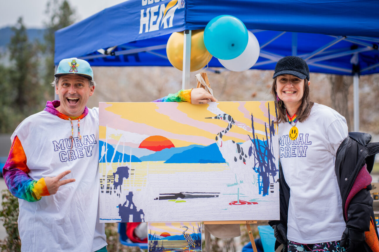 Two individuals holding up a mural painting at UBC Giving Day event.