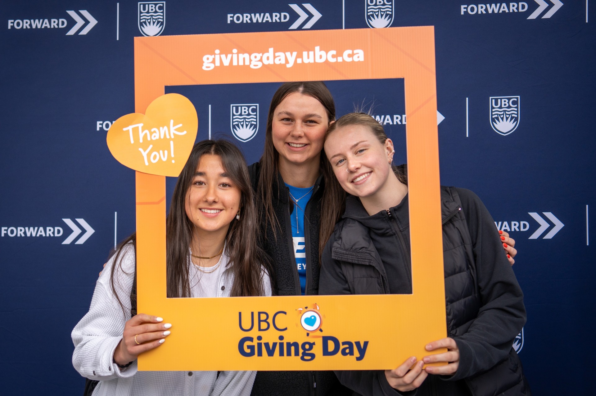 Three volunteers posing with photo frame at UBC Giving Day event.